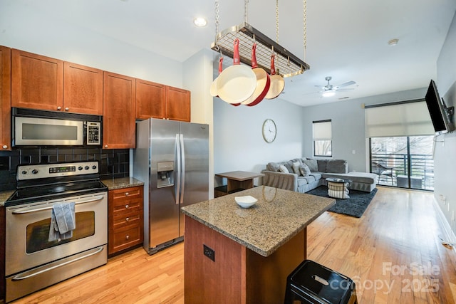 kitchen featuring light hardwood / wood-style flooring, backsplash, a center island, stainless steel appliances, and light stone countertops