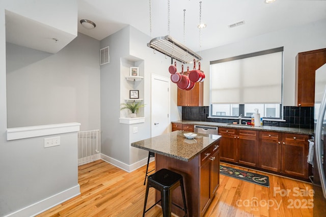 kitchen featuring light wood-type flooring, a center island, a breakfast bar, tasteful backsplash, and dark stone counters