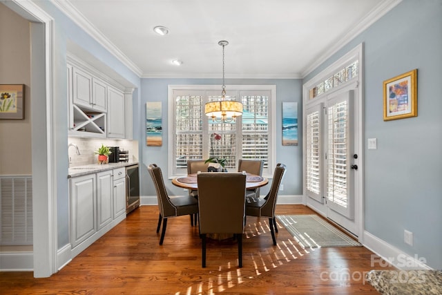 dining area with an inviting chandelier, hardwood / wood-style flooring, sink, and ornamental molding