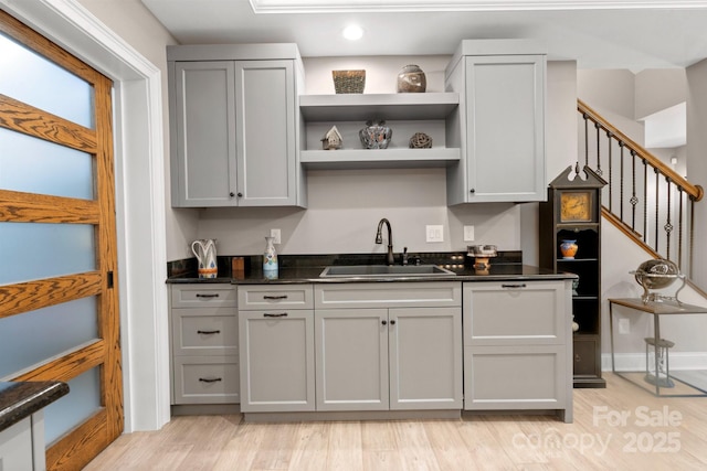 kitchen with sink, dark stone counters, gray cabinetry, and light wood-type flooring