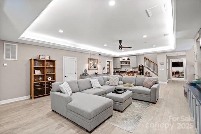 living room featuring a tray ceiling, ceiling fan, and light hardwood / wood-style flooring