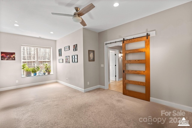 empty room featuring ceiling fan, a barn door, and light colored carpet