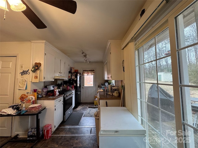 kitchen with black refrigerator, stainless steel gas range, white cabinets, and track lighting