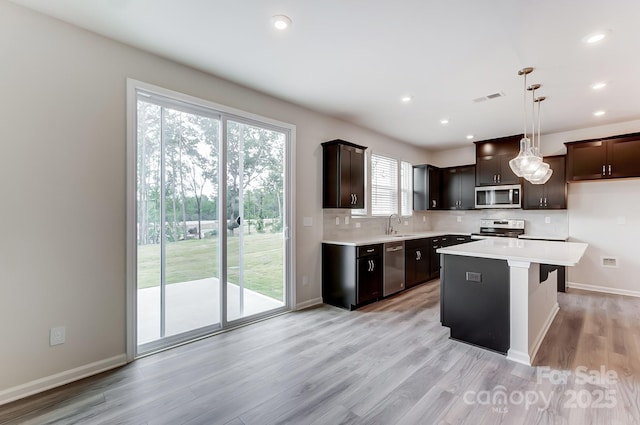 kitchen with sink, appliances with stainless steel finishes, backsplash, a kitchen island, and decorative light fixtures