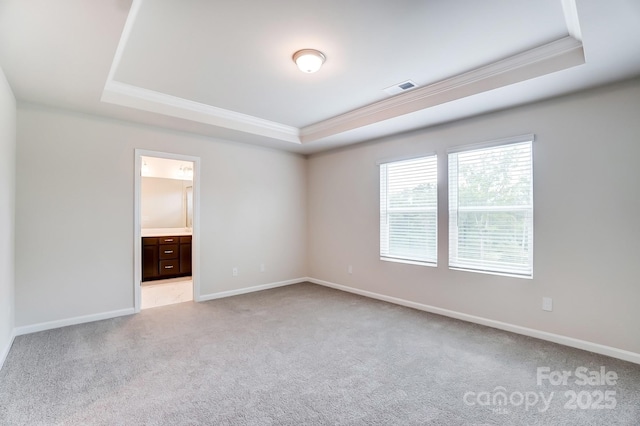 empty room featuring a tray ceiling, ornamental molding, and light colored carpet