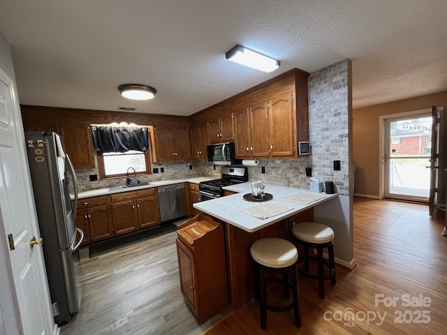 kitchen with a kitchen bar, sink, light hardwood / wood-style flooring, kitchen peninsula, and stainless steel appliances