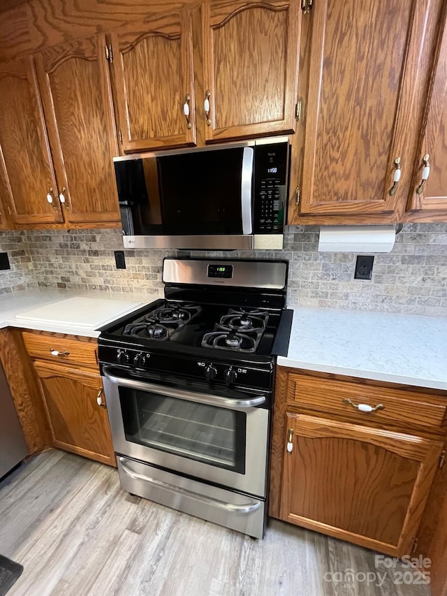 kitchen with tasteful backsplash, appliances with stainless steel finishes, and light hardwood / wood-style floors