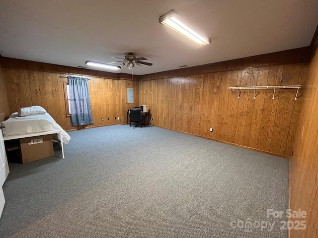 basement featuring ceiling fan, wooden walls, electric panel, and carpet