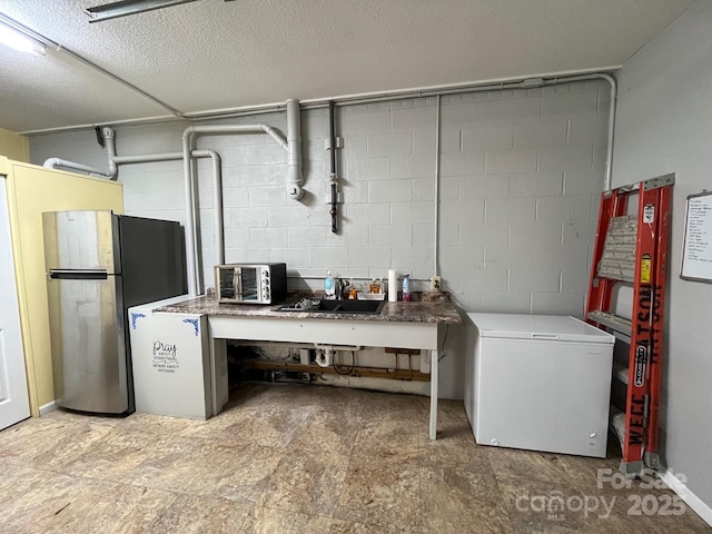 basement featuring fridge, sink, stainless steel fridge, and a textured ceiling