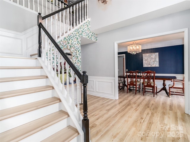 staircase featuring a chandelier, a wainscoted wall, wood finished floors, and a decorative wall