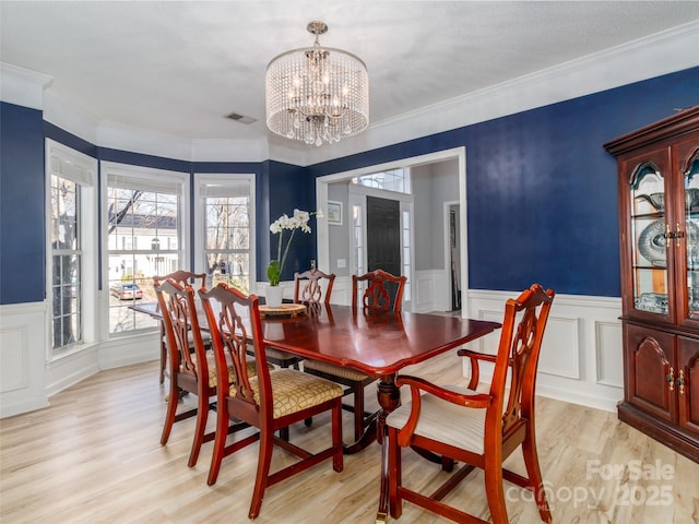 dining space featuring a chandelier, a wainscoted wall, visible vents, light wood finished floors, and crown molding