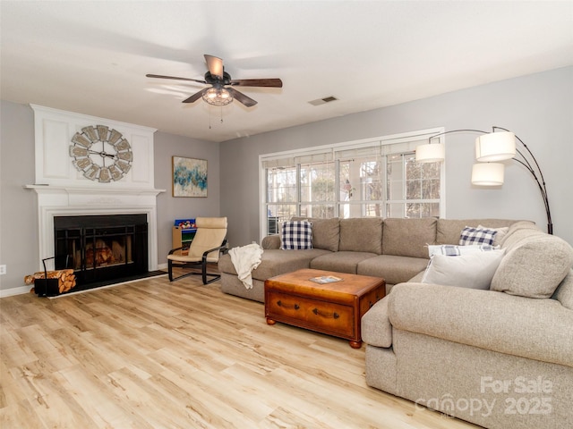 living area featuring visible vents, baseboards, ceiling fan, light wood-type flooring, and a fireplace