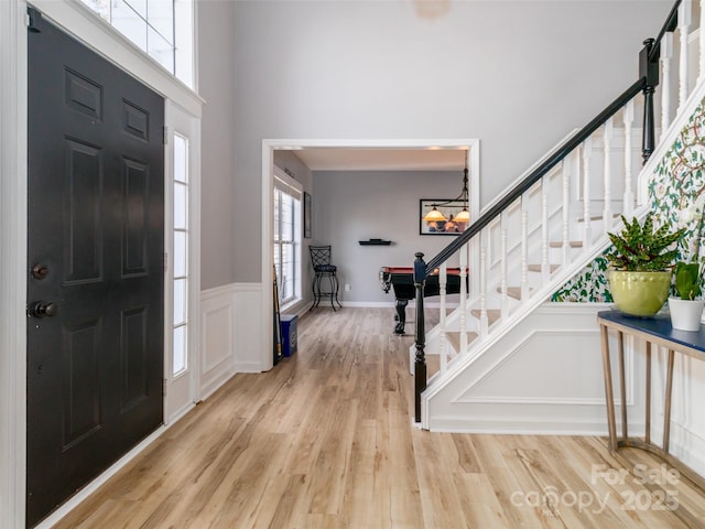 foyer with a wainscoted wall, light wood finished floors, a decorative wall, a towering ceiling, and stairway