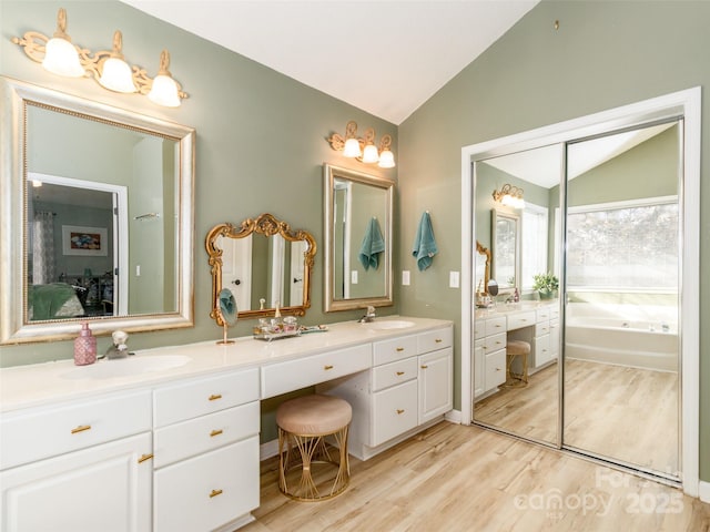 ensuite bathroom featuring lofted ceiling, a sink, ensuite bath, and wood finished floors