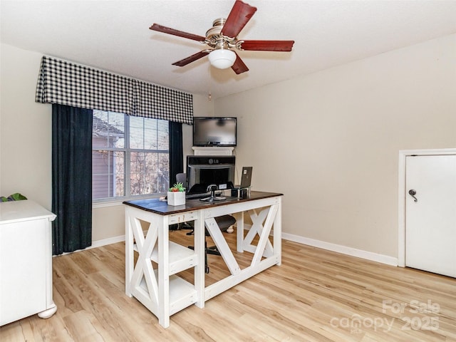 home office featuring light wood finished floors, a ceiling fan, and baseboards