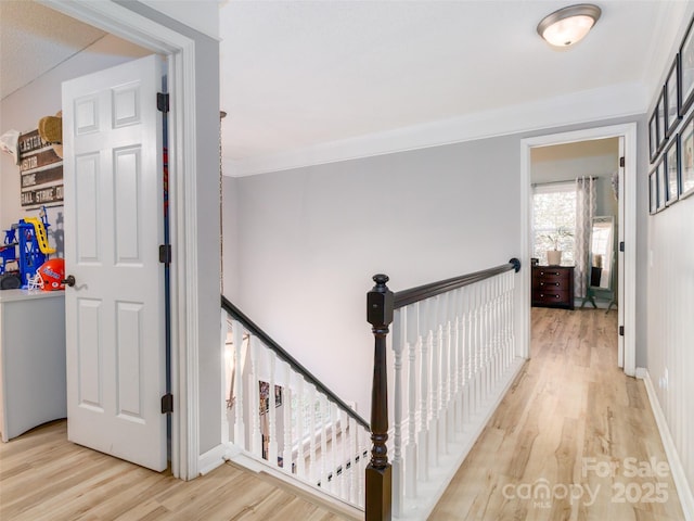 hall with baseboards, crown molding, light wood finished floors, and an upstairs landing