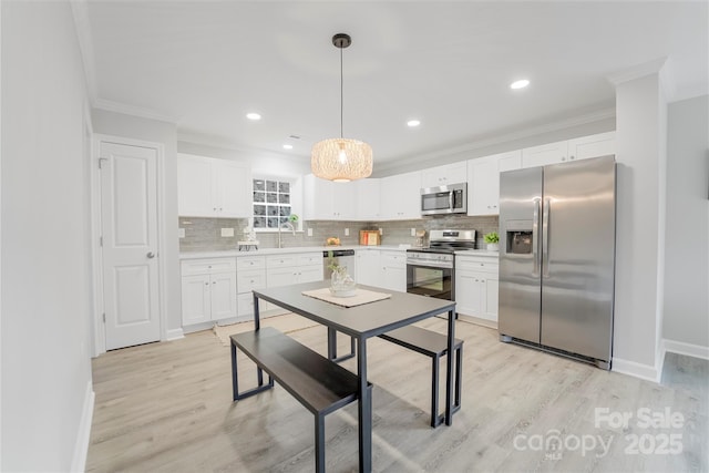 kitchen featuring crown molding, appliances with stainless steel finishes, white cabinets, and decorative light fixtures