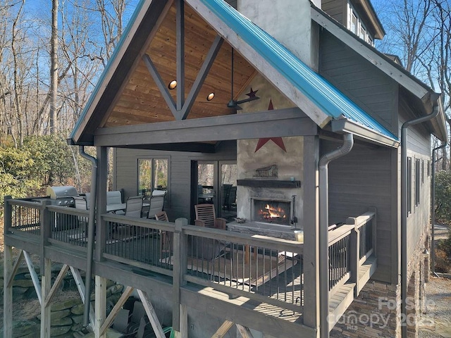 exterior space with a wooden deck, an outdoor fireplace, and ceiling fan