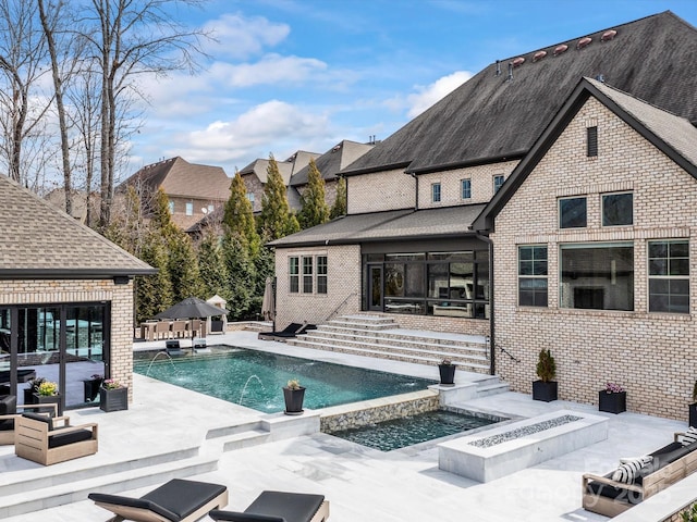 back of property featuring roof with shingles, an in ground hot tub, an outdoor pool, a patio area, and brick siding