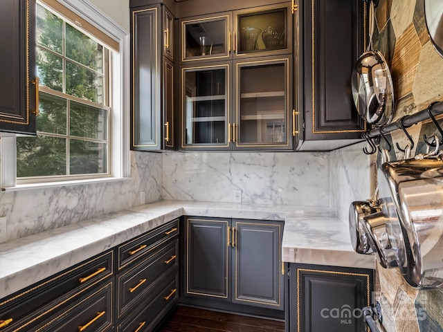 kitchen with glass insert cabinets, light stone countertops, tasteful backsplash, and dark wood-style floors