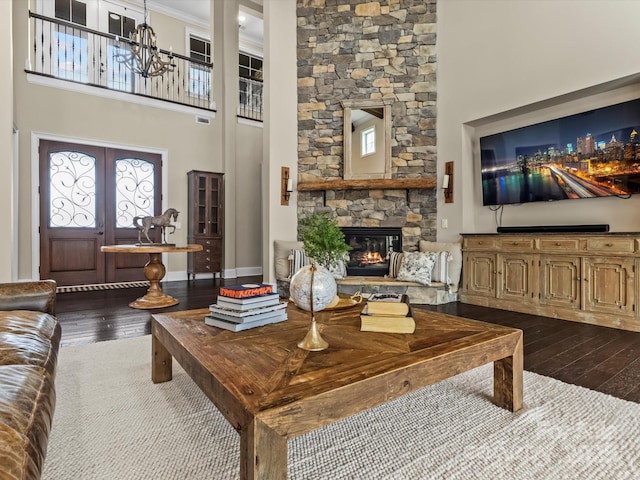 living area with a high ceiling, a notable chandelier, dark wood-type flooring, and a stone fireplace