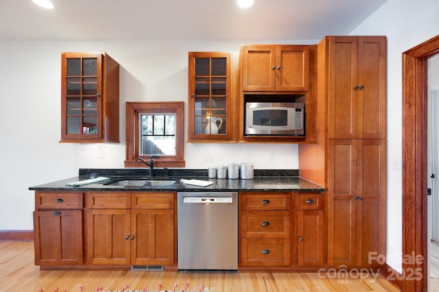 kitchen featuring dark stone countertops, sink, light wood-type flooring, and appliances with stainless steel finishes