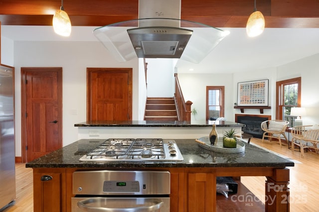 kitchen with appliances with stainless steel finishes, decorative light fixtures, light wood-type flooring, and dark stone counters