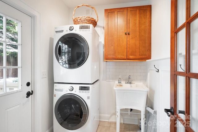 clothes washing area with stacked washer / drying machine, light tile patterned floors, and cabinets