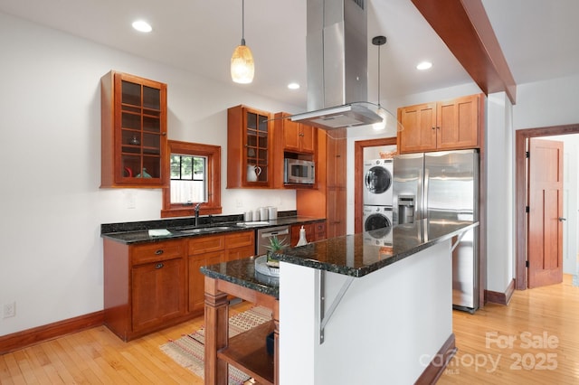 kitchen featuring island range hood, stacked washer / dryer, sink, hanging light fixtures, and stainless steel appliances