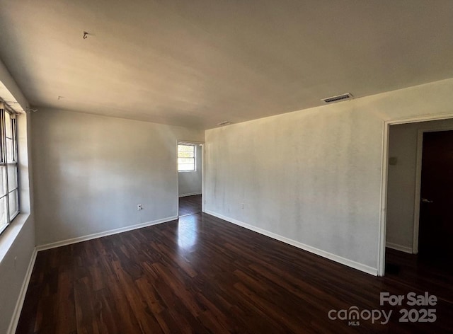 unfurnished room featuring dark wood-type flooring, visible vents, and baseboards