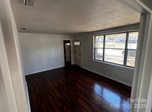 empty room with visible vents, dark wood finished floors, and baseboards