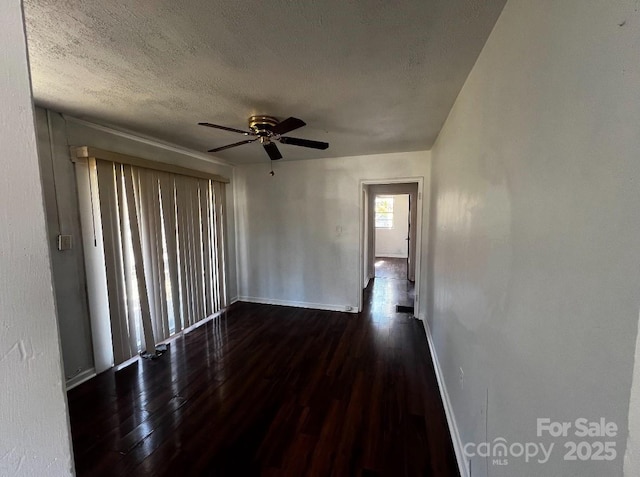 unfurnished room with a textured ceiling, ceiling fan, dark wood-type flooring, and baseboards