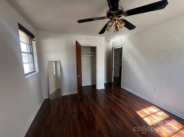 unfurnished bedroom with dark wood finished floors, a textured wall, and baseboards