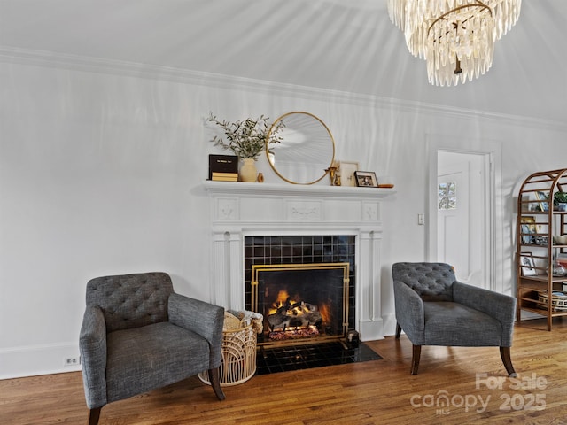 living area with a tile fireplace, crown molding, hardwood / wood-style flooring, and an inviting chandelier