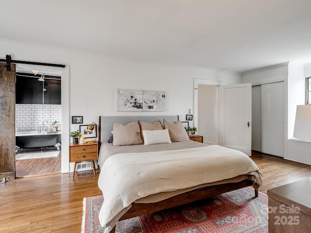 bedroom featuring crown molding, wood-type flooring, and a barn door