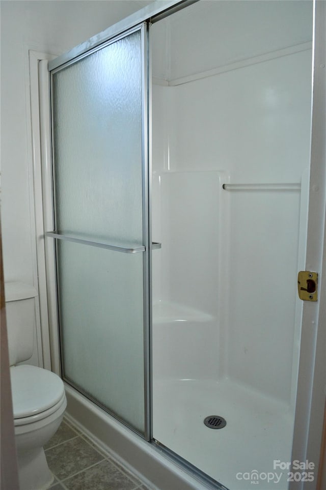 bathroom with tile patterned flooring, toilet, and a shower with shower door