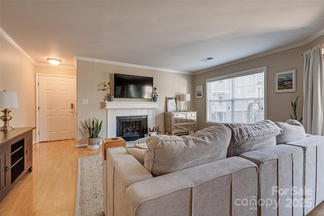 living room featuring a tile fireplace, ornamental molding, and light wood-type flooring