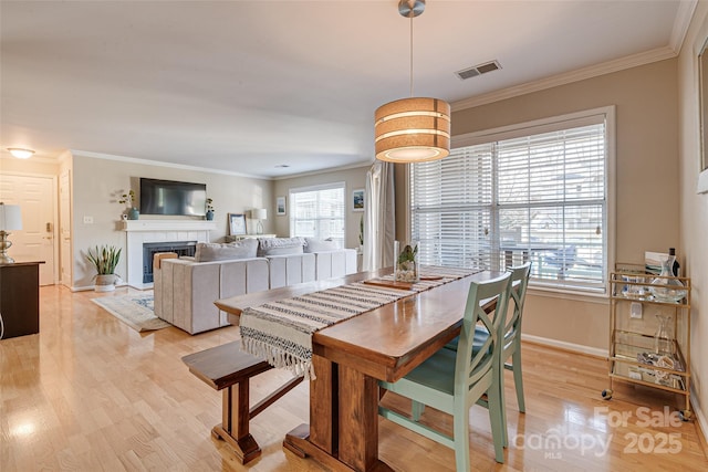 dining area with a tiled fireplace, ornamental molding, and light hardwood / wood-style flooring