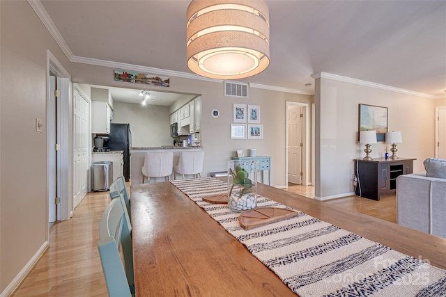 dining area with ornamental molding and light hardwood / wood-style flooring