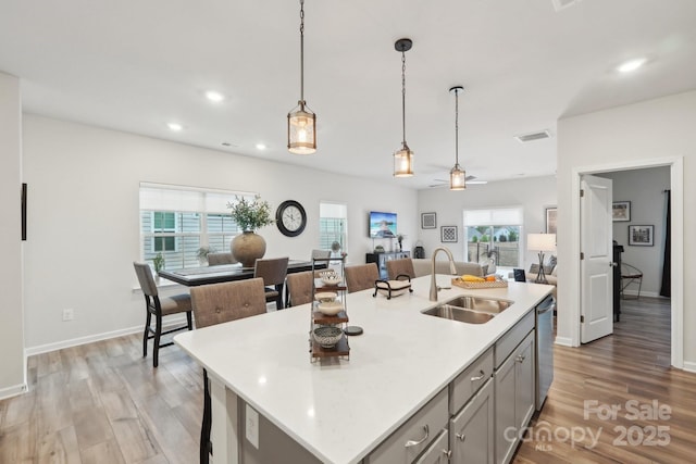 kitchen with decorative light fixtures, dishwasher, sink, gray cabinetry, and a kitchen island with sink