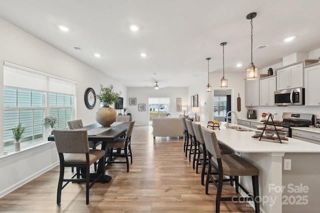 dining room featuring a breakfast bar, sink, decorative light fixtures, light wood-type flooring, and a large island with sink