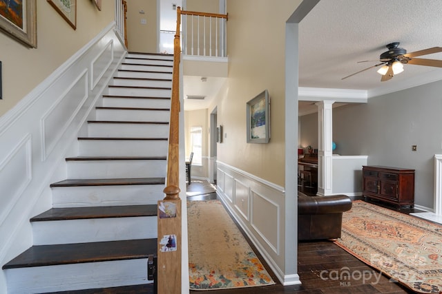 staircase with crown molding, wood-type flooring, a textured ceiling, ceiling fan, and decorative columns