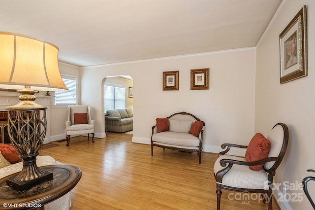 sitting room featuring ornamental molding, baseboards, light wood-type flooring, and arched walkways