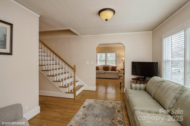 living area with arched walkways, baseboards, ornamental molding, and wood finished floors