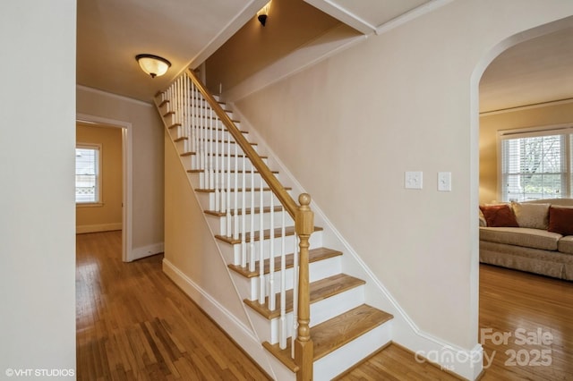 staircase with a wealth of natural light, arched walkways, and wood finished floors