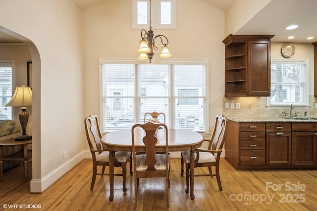 dining space with baseboards, light wood-type flooring, arched walkways, and lofted ceiling