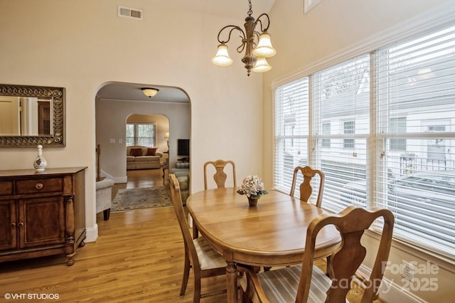 dining space featuring visible vents, baseboards, arched walkways, a notable chandelier, and light wood-style flooring