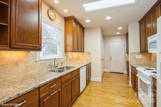 kitchen with light wood-type flooring, baseboards, white appliances, light stone countertops, and a sink