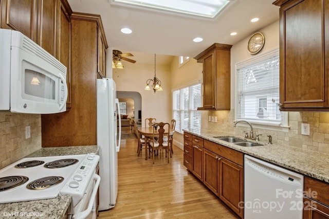 kitchen with tasteful backsplash, a sink, white appliances, brown cabinets, and light wood-style flooring