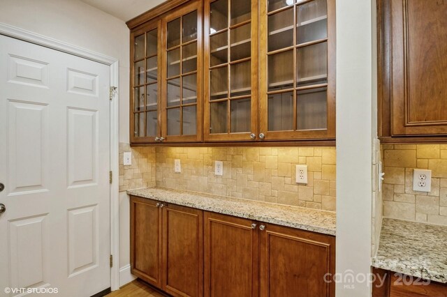 kitchen with brown cabinets, glass insert cabinets, decorative backsplash, and light stone countertops